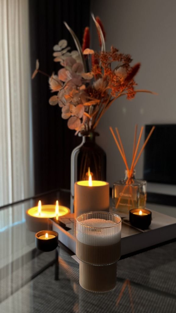 Warm and stylish home decor setup with candles and dried flowers on a glass table.